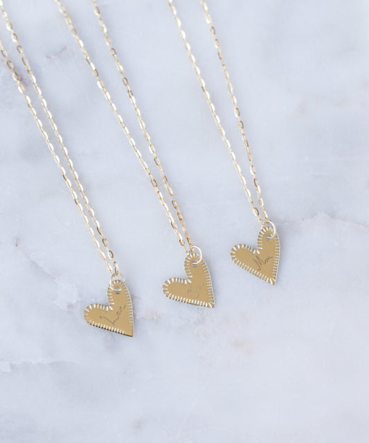 Three WALD Berlin "Be My Lover Heart" 18k gold pendants, crafted in Germany, are displayed side by side on delicate chains atop a white marble surface.