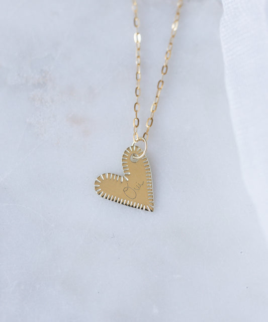 The WALD Berlin Be My Lover Heart 18k Pendant Without Chain features stitched-edge details and "love" engraving, elegantly displayed on white marble. This German-made jewelry piece exudes sophistication.