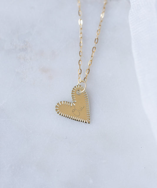 The WALD Berlin Be My Lover Heart 18k Pendant Without Chain features stitched-edge details and "love" engraving, elegantly displayed on white marble. This German-made jewelry piece exudes sophistication.