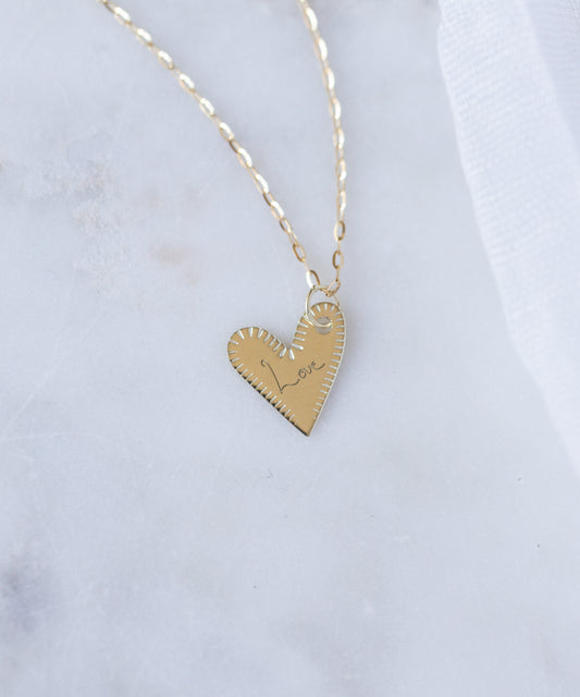 The WALD Berlin Be My Lover Heart 18k Pendant Without Chain—timeless engraved jewelry crafted in Germany—rests on a white marble surface.