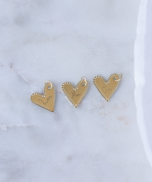 Three WALD Berlin "Be My Lover Heart" 18k gold pendants without chains are displayed on white marble, highlighting the timeless elegance of engraved jewelry.