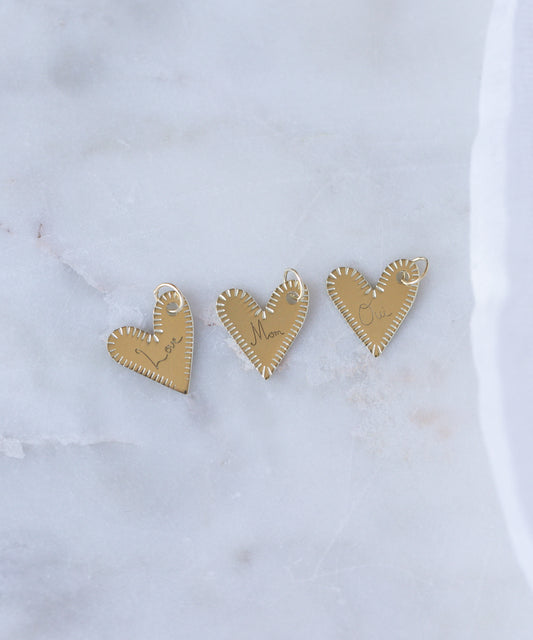 Three WALD Berlin "Be My Lover Heart" 18k gold pendants without chains are displayed on white marble, highlighting the timeless elegance of engraved jewelry.