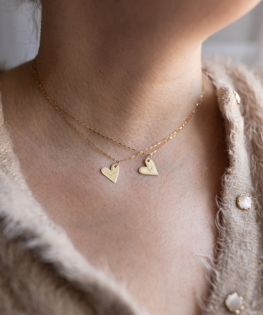 Close-up of a person in a fuzzy beige sweater wearing two gold necklaces, including WALD Berlin's Be My Lover Heart 18k Pendant Without Chain. Each heart-shaped pendant enhances the elegance of this look.