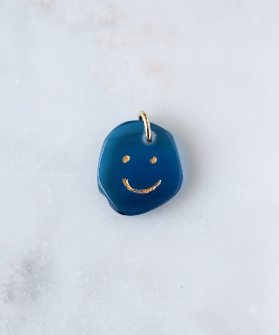 The WALD Berlin Smilie Dude Gemstone Pendant Without Chain features a small blue charm with a gold smiling face and metal loop, made in Germany—an elegant accent for any 18k gold necklace.