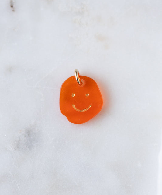 The WALD Berlin Smilie Dude Gemstone Pendant Without Chain features an orange, irregular-shaped charm with a simple smiley face and a metal loop—ideal for adding personality to your favorite 18k gold necklace.