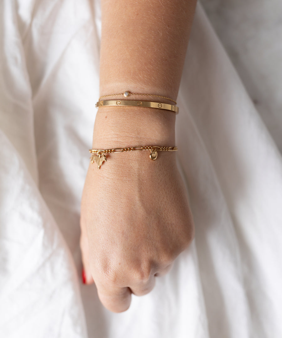 A wrist showcases three 18k gold plated bracelets, including the WALD Berlin SAMPLE SALE Charm Bracelet Z Edition with a delicate charm, elegantly resting on a white fabric background.