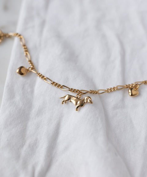 The SAMPLE SALE Charm Bracelet Z Edition by WALD Berlin, an 18k gold-plated chain with heart and dachshund charms, is shown on a white fabric background.