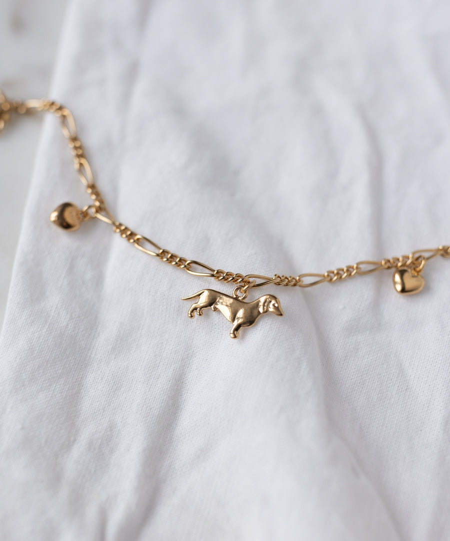 The SAMPLE SALE Charm Bracelet Z Edition by WALD Berlin, an 18k gold-plated chain with heart and dachshund charms, is shown on a white fabric background.