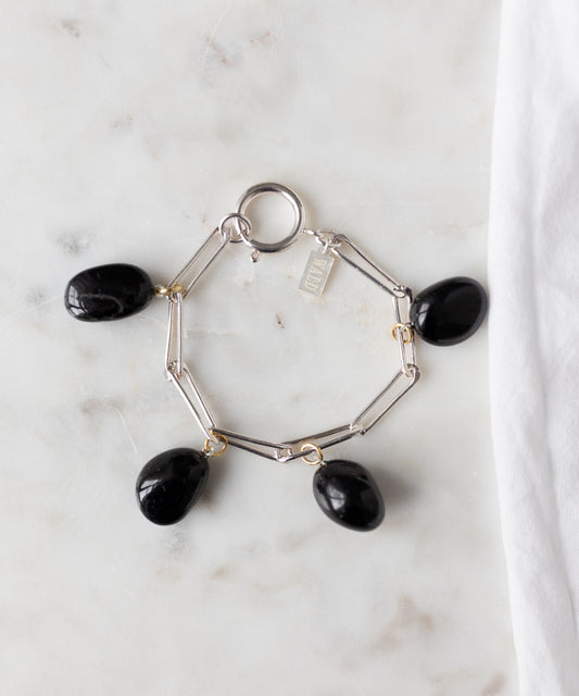 The WALD Berlin Collection Noir Ashley Drop Silver Bracelet features four black oval stone charms and a small rectangular tag, crafted from recycled silver and displayed on white marble.