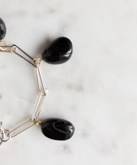 The WALD Berlin Collection Noir Ashley Drop Silver Bracelet, made from recycled silver and featuring three large black stone charms, rests on a white marble surface.