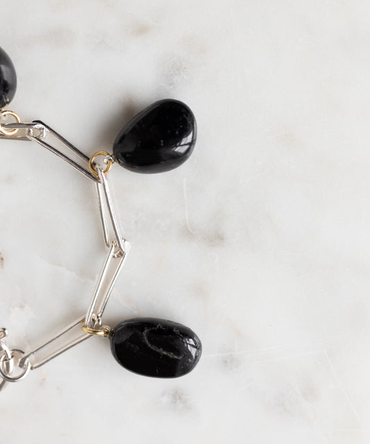 The WALD Berlin Collection Noir Ashley Drop Silver Bracelet, made from recycled silver and featuring three large black stone charms, rests on a white marble surface.