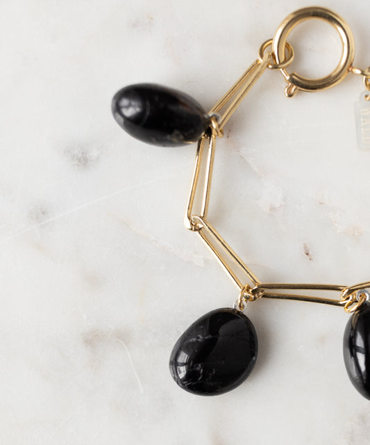 The Collection Noir Ashley Drop Gold Bracelet by WALD Berlin features three oval black stone charms, shown on a white marble surface.