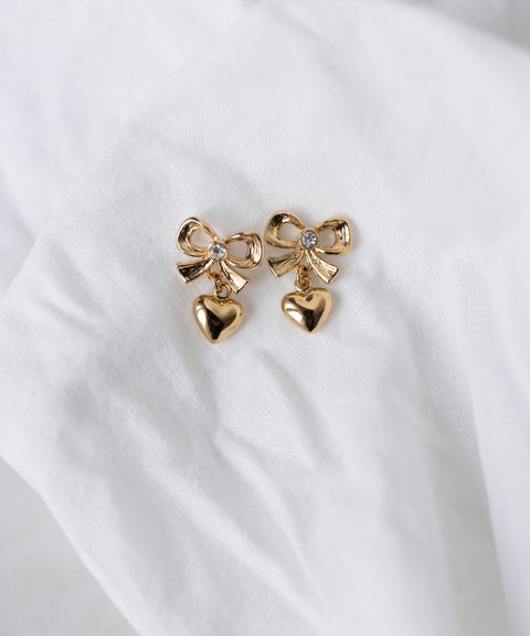WALD Berlin's Valentines Day special bow heart earrings—gold-plated brass with bow designs and dangling heart charms—are shown on a white fabric background. Perfect as heart earrings for Valentine's Day.