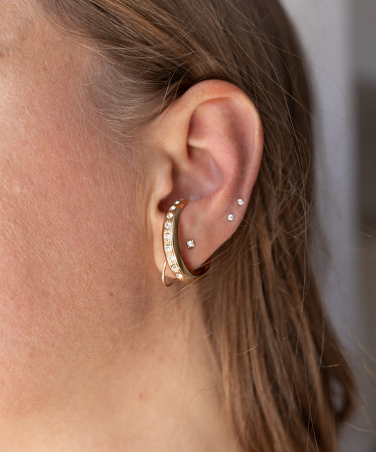 Gold-plated Hug Me Earcuff set by WALD Berlin with small crystals worn on the side of a human ear.