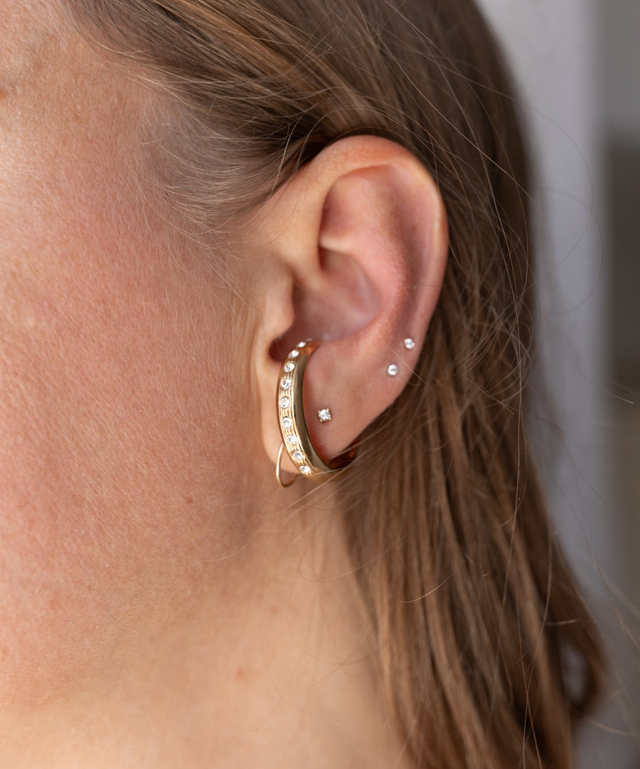 Gold-plated Hug Me Earcuff set by WALD Berlin with small crystals worn on the side of a human ear.