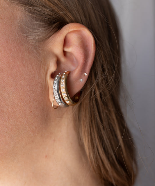 A person wearing a silver-toned crystal-embellished earcuff and a gold-plated Hug Me Earcuff Gold stacked in the conch of their ear.