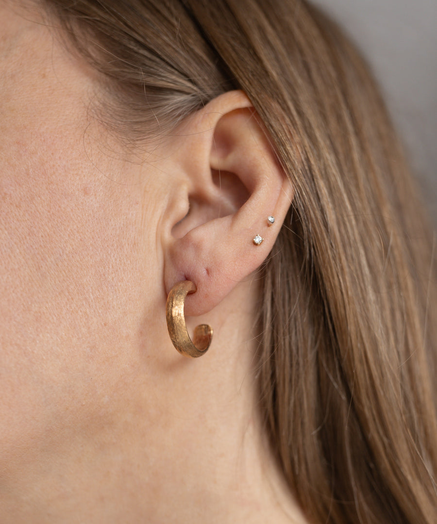 Close-up of an ear with three small studs on the upper ear and the WALD Berlin SAMPLE SALE Pop Classy Hoop Gold earring on the lobe—don’t miss it at our sample sale!.