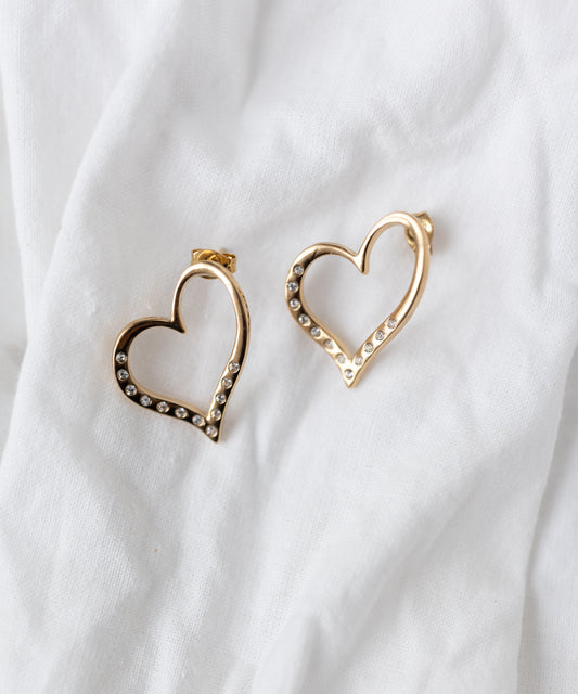 The WALD Berlin Valentines Day special sketch heart earrings feature 18k gold plating and Swarovski stones, shown on a white fabric background.