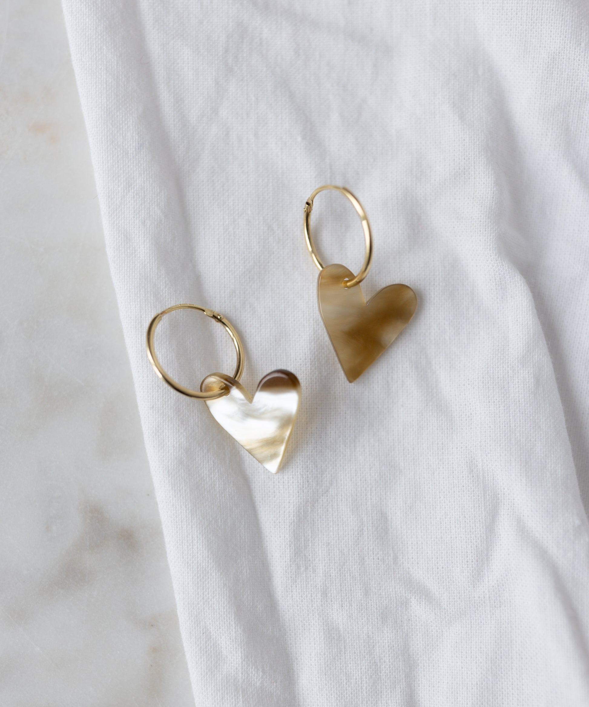 The WALD Berlin Exclusive Heart Black Earrings, featuring recycled gold hoops with heart-shaped pendants, are displayed on a white fabric surface.