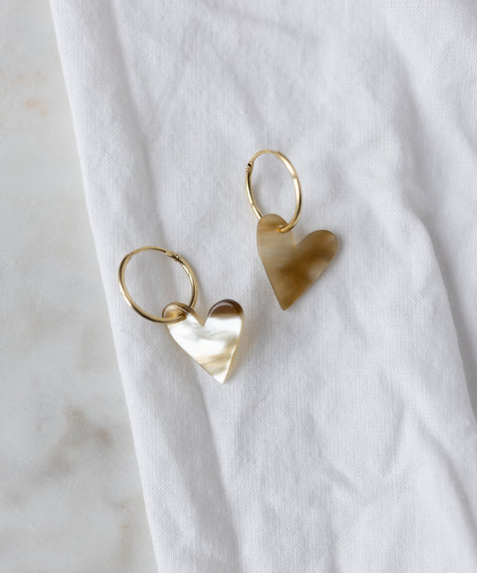 The WALD Berlin Exclusive Heart Black Earrings, featuring recycled gold hoops with heart-shaped pendants, are displayed on a white fabric surface.