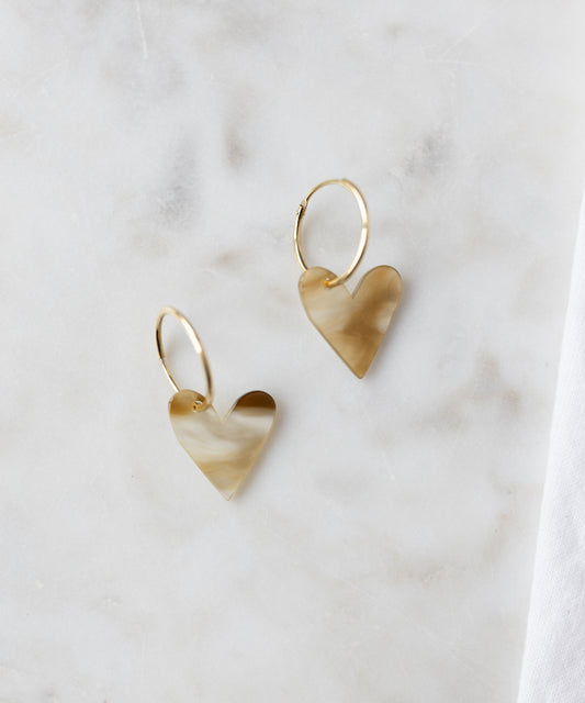 The WALD Berlin Exclusive Heart Black Earrings feature recycled gold hoops with marbled black heart-shaped pendants, elegantly displayed on a light marble surface.