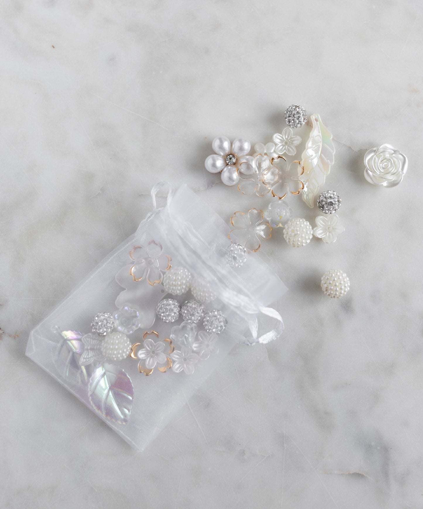 The WALD Berlin Candyman Pearl Kit is a sheer white drawstring bag filled with assorted pearly beads, floral shapes, and leaf ornaments—an elegant DIY kit inspired by designer Dana Roski’s signature style.