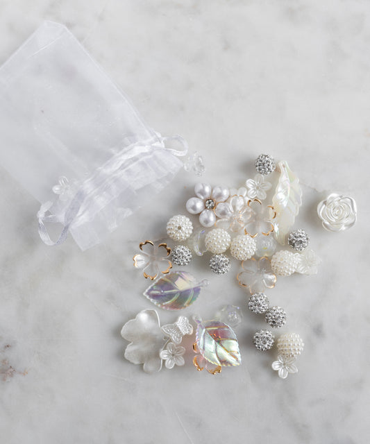 The WALD Berlin Candyman Pearl Kit is a sheer white drawstring bag adorned with decorative white and silver beads, pearly beads, faux pearls, flowers, and leaves—a delicate piece inspired by designer Dana Roski.