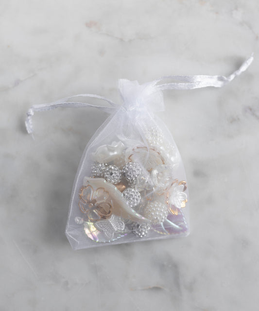 The WALD Berlin Candyman Pearl Kit, a small sheer white drawstring bag filled with assorted pearly beads and embellishments, rests elegantly on a light marble surface.
