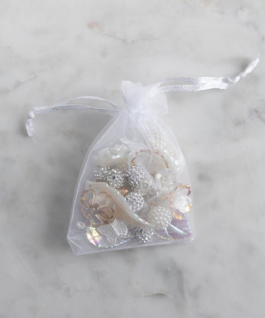 The WALD Berlin Candyman Pearl Kit, a small sheer white drawstring bag filled with assorted pearly beads and embellishments, rests elegantly on a light marble surface.