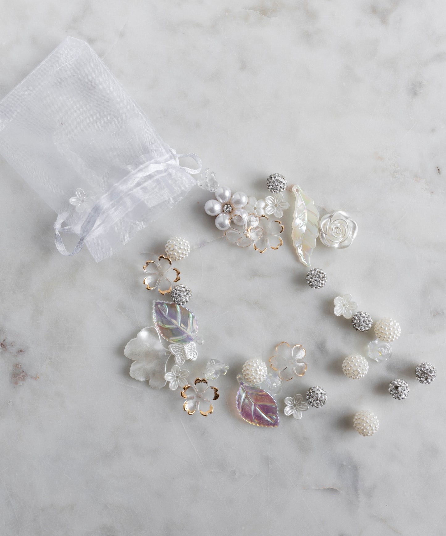 The Candyman Pearl Kit by WALD Berlin is a sheer white drawstring bag featuring pearly beads and floral details, artfully displayed on a marble surface.