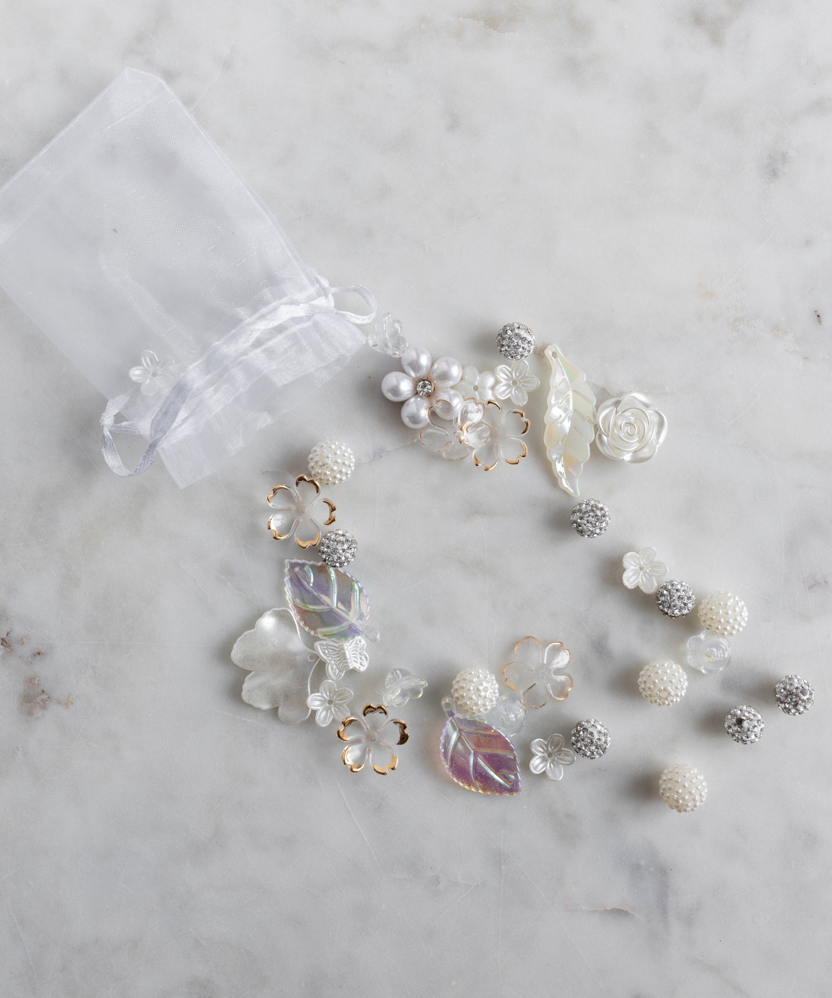 The Candyman Pearl Kit by WALD Berlin is a sheer white drawstring bag featuring pearly beads and floral details, artfully displayed on a marble surface.