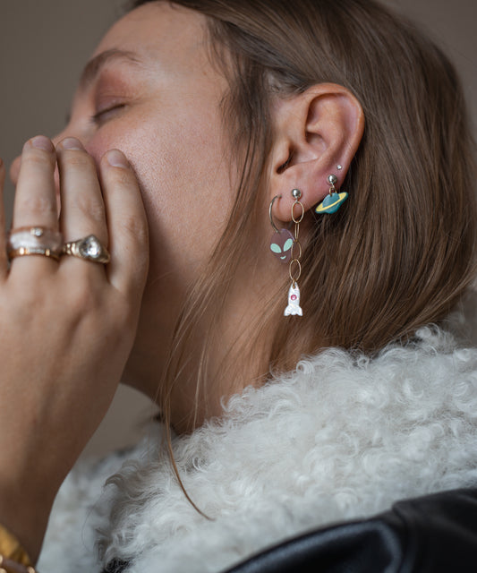 Wearing the WALD Berlin SAMPLE SALE From Another Mother Galactic Earring Set—space-themed 925 sterling silver—a person with long hair and rings dons a white furry bio polyester jacket.