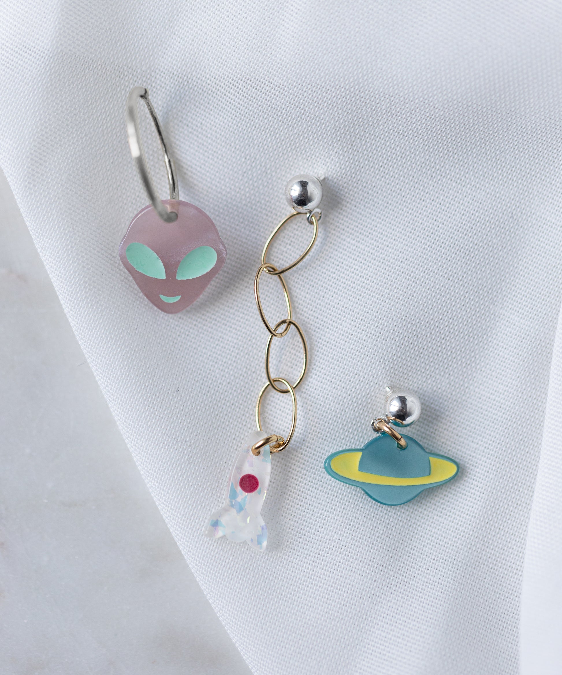 The SAMPLE SALE From Another Mother Galactic Earring Set by WALD Berlin features three bio polyester and 925 sterling silver earrings: a purple alien face, a rocket charm on gold chain, and a blue-yellow planet charm.