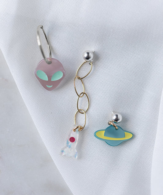 The SAMPLE SALE From Another Mother Galactic Earring Set by WALD Berlin features three bio polyester and 925 sterling silver earrings: a purple alien face, a rocket charm on gold chain, and a blue-yellow planet charm.