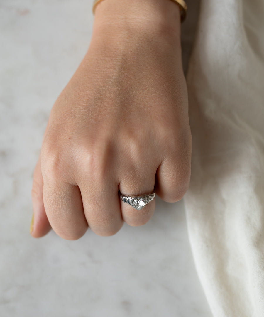 Close-up of a woman's clenched fist resting on a marble surface, showcasing a WALD Berlin Be My Lover Mini Silver Ring with a large round gemstone.