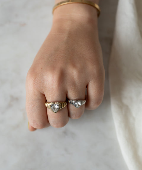 A close-up image of a hand wearing two detailed rings, one Be My Lover Mini Silver Ring by WALD Berlin and one gold, resting on a marble surface.