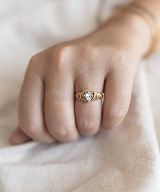 A woman's hand holding a "Be My Lover Ring Mini" by WALD Berlin, with a diamond in the center, accentuated by a Swarovski stone.