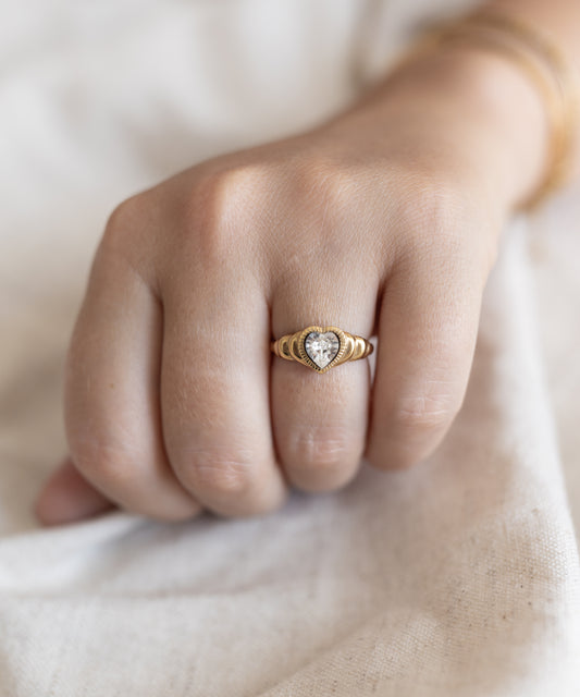 A woman's hand holding a "Be My Lover Ring Mini" by WALD Berlin, with a diamond in the center, accentuated by a Swarovski stone.