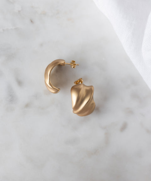 SAMPLE SALE Matt Gold Creoles by WALD Berlin—18k gold plated, abstract-shaped earrings made in Germany—displayed on white marble with a white cloth in the corner.