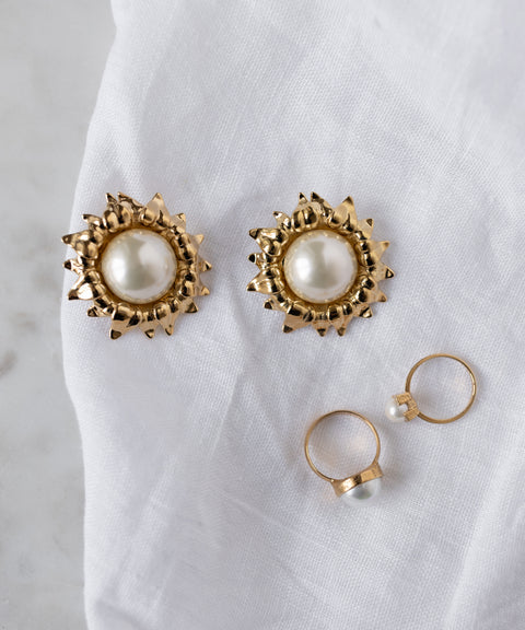 A pair of gold and pearl stud earrings and two WALD Berlin SAMPLE SALE Pop Pearl Ring Minis, crafted from gold-plated brass, displayed on a white fabric surface.