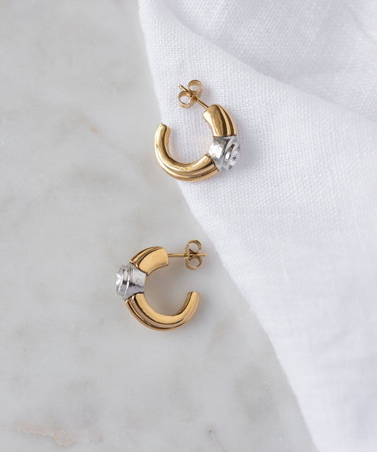 The SAMPLE SALE Pop Bi Color Crystal Earrings by WALD Berlin, with gold and silver tones, are displayed on a white marble surface partially covered by a white cloth.