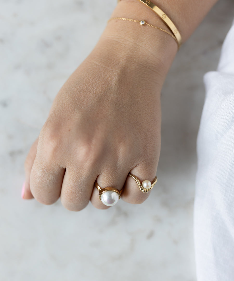 A hand wearing an 18k gold-plated bracelet and two WALD Berlin rings—one is the SAMPLE SALE Pop Pearl Ring with a large pearl, the other features a small pearl—set against a light background.