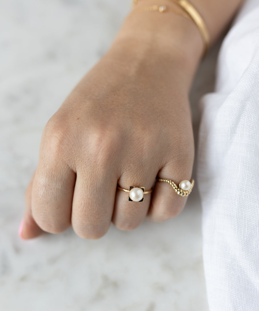 A hand adorned with two WALD Berlin SAMPLE SALE Pop Pearl Ring Minis—crafted from gold plated brass in Germany—rests elegantly on a white surface beside a gold bracelet.