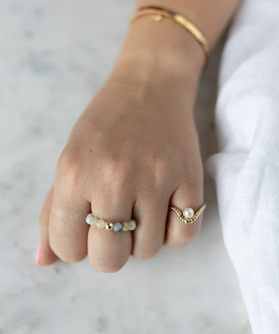 A hand adorned with the WALD Berlin Pop Gemstone Ring Set and a gold bracelet rests on a light surface—elegant gift ideas, especially with flexible size options for the perfect fit.