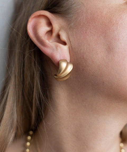 Close-up of a person wearing WALD Berlin’s SAMPLE SALE Matt Gold Creoles on their left ear. Straight hair is partially visible.