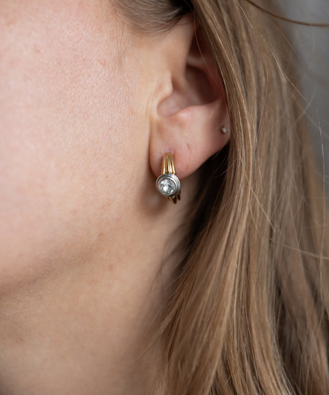 Close-up of a person's ear wearing WALD Berlin SAMPLE SALE Pop Bi Color Crystal Earrings; gold plated with Swarovski stone, hair partially covers the side of the face.