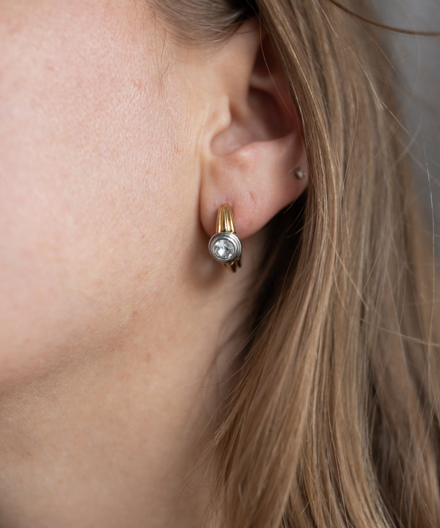 Close-up of a person's ear wearing WALD Berlin SAMPLE SALE Pop Bi Color Crystal Earrings; gold plated with Swarovski stone, hair partially covers the side of the face.