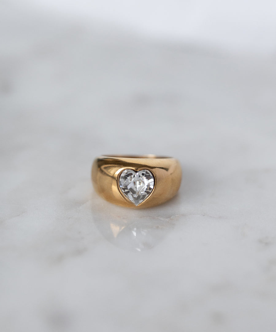 The WALD Berlin Mom Swarovski Heart Ring, adorned with a sparkling heart-shaped Swarovski stone, rests elegantly on a light marble surface.