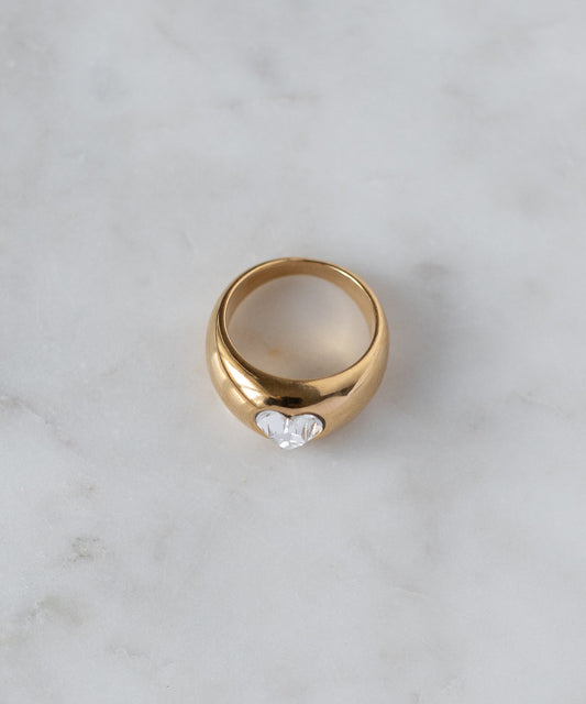 The WALD Berlin Mom Swarovski Heart Ring, gold plated with a single clear Swarovski stone at the center, is displayed on a light marble surface.