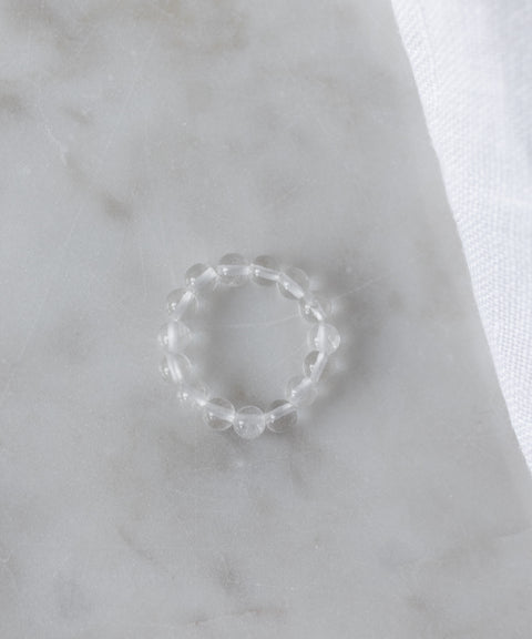 The Pop Gemstone Ring Set by WALD Berlin features a clear beaded ring with an adjustable fit, displayed on white marble beside soft fabric—perfect for unique gift ideas.